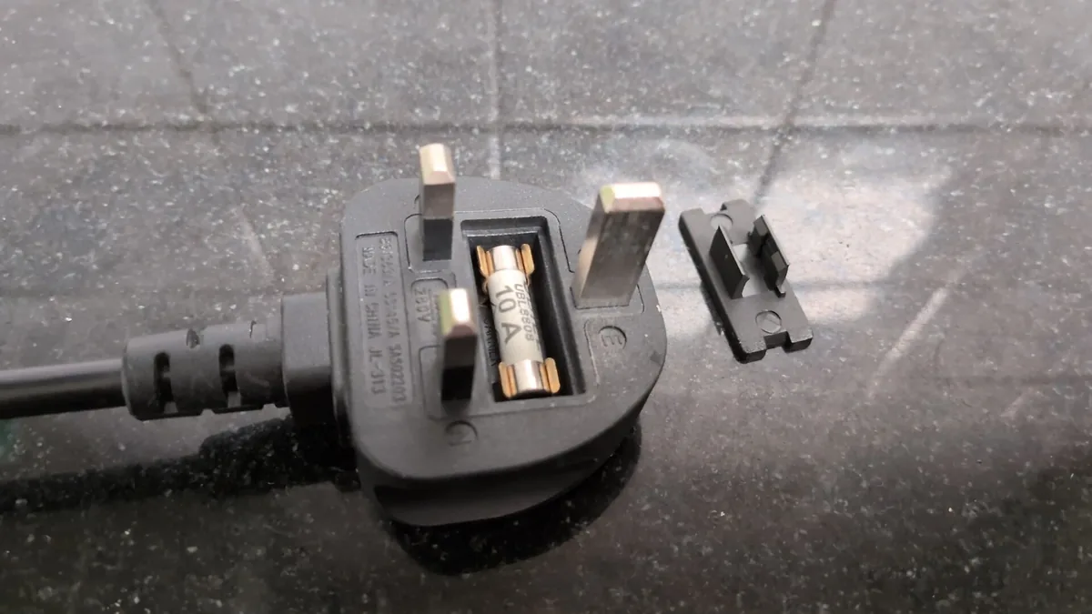 Open fuse compartment of a black UK plug: ceramic fuse marked 10 A in brass clips